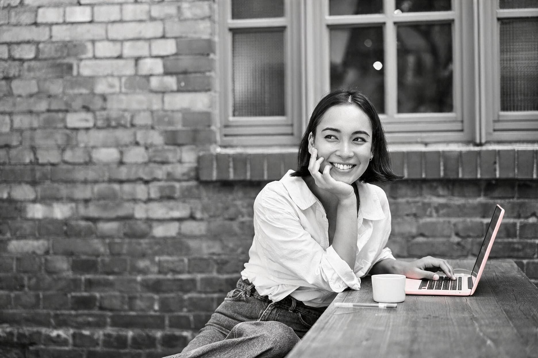 A young woman smiling at a table with a pink laptop