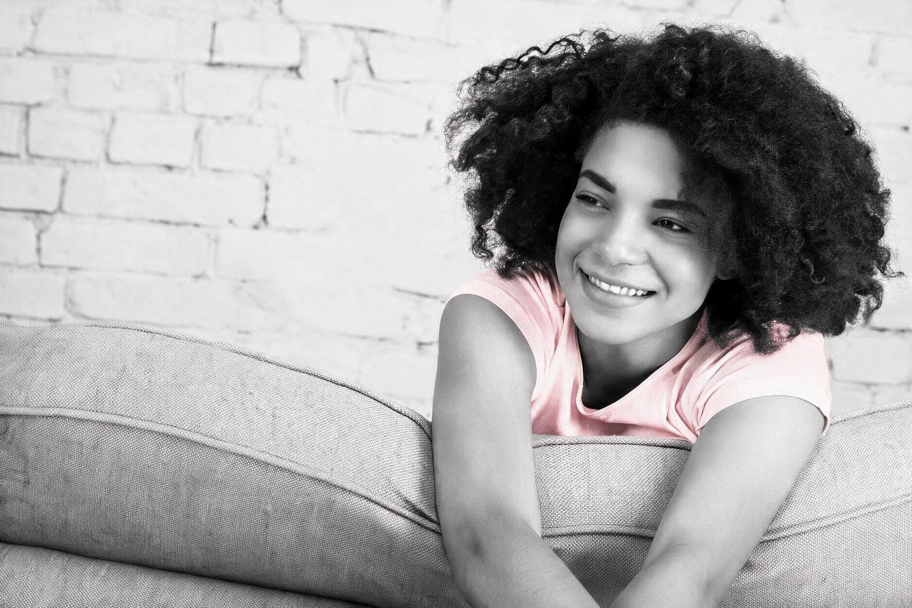 A girl in a pale pink t-shirt smiling, resting on a sofa