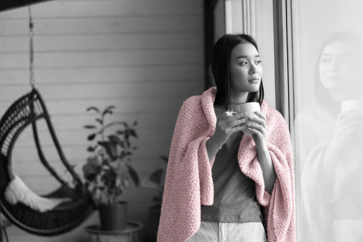 A young woman wrapped in a pink blanket looking out a window